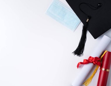 Mezuniyet karesi akademik şapkasının üst görünümü diploma ve maske beyaz masa arkasında izole.