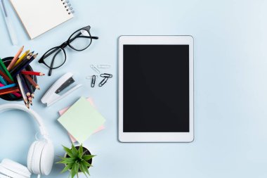 Çevrimiçi öğrenim tasarımı. Tabletli, kulaklıklı ve mavi masa arkaplanlı öğrenci tablosunun üst görünümü.