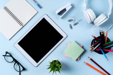 Çevrimiçi öğrenim tasarımı. Tabletli, kulaklıklı ve mavi masa arkaplanlı öğrenci tablosunun üst görünümü.