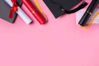Mezuniyet karesi akademik şapkası diploması ve maskesi pembe masa arkasında izole..