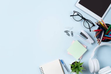 Çevrimiçi öğrenim tasarımı. Tabletli, kulaklıklı ve mavi masa arkaplanlı öğrenci tablosunun üst görünümü.