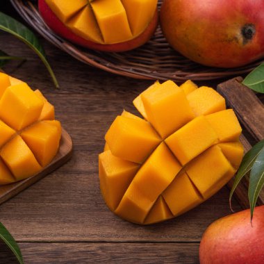 Mango. Taze olgun mango meyvelerini koyu ahşap masa zemininde yeşil yapraklarla kaplayın..