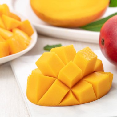 Tahta masa arkasında yaprakları olan beyaz bir tabakta doğranmış taze mango meyvesi..