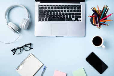 Çevrimiçi öğrenim tasarımı. Bilgisayarlı, kulaklıklı ve mavi masa arkaplanlı öğrenci tablosunun üst görünümü.