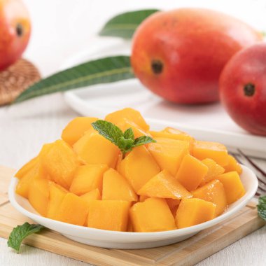 Tahta masa arkasında yaprakları olan beyaz bir tabakta doğranmış taze mango meyvesi..