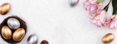 Yuvadaki altın ve gümüş Paskalya yumurtalarının tasarımı. Pembe zambak çiçekli parlak mermer masa arkaplanı..