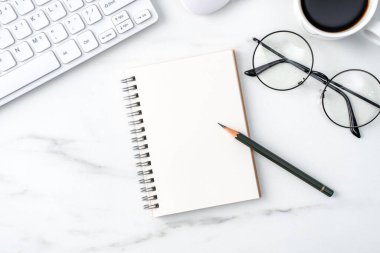 Klavye, defter, kalem, gözlük ve kahveyle birlikte parlak mermer beyaz arka planda ofis masası rahat çalışma konsepti.