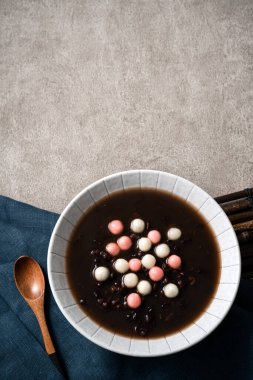 Kırmızı ve beyaz tangyuan 'ın (tang yuan, glutinous rice dumpling balls) en üst görüntüsü. Gri masa üzerinde tatlı kırmızı fasulye çorbası ile kış gündönümü festivali yemekleri için..