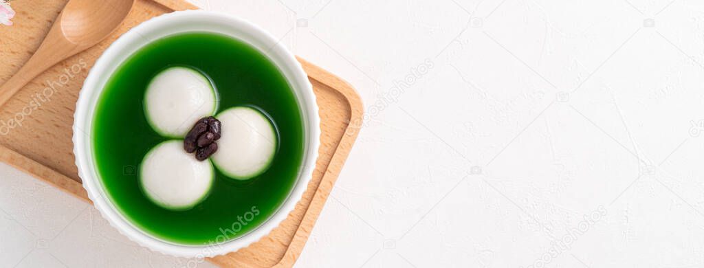 Top view of matcha big tangyuan (tang yuan) with sweet matcha soup and red bean paste in a bowl on white table background for festival food.