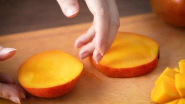 Kadın taze mango meyvesi kesiyor ve ev mutfağında yemek için doğranmış hamurun sulu tarafını gösteriyor..
