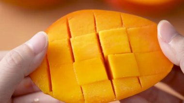 Kadın taze mango meyvesi kesiyor ve ev mutfağında yemek için doğranmış hamurun sulu tarafını gösteriyor..
