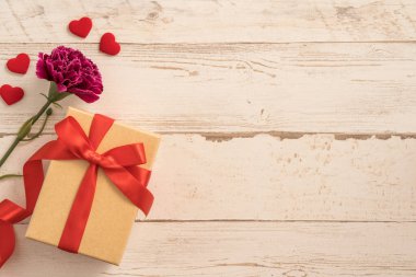 Kırmızı kurdele ve karanfilli Kraft hediye kutusu. Anneler gününde hediye verme konsepti. Sürpriz, düz yatak, üst manzara.