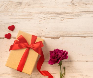 Kırmızı kurdele ve karanfilli Kraft hediye kutusu. Anneler gününde hediye verme konsepti. Sürpriz, düz yatak, üst manzara.