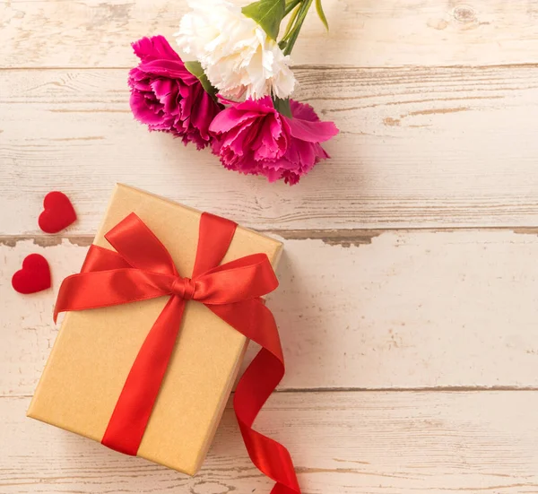 Kırmızı kurdele ve karanfilli Kraft hediye kutusu. Anneler gününde hediye verme konsepti. Sürpriz, düz yatak, üst manzara.