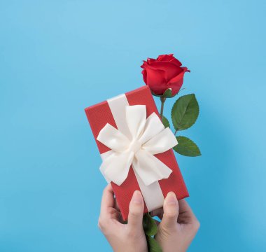 Genç bir kadın, bayram konsepti olan mavi arkaplanlı bir hediye veriyor ve festival için sürpriz, fotokopi alanı, üst görünüm için kutlama yapıyor.