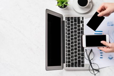 Bir kadın çevrimiçi ödeme ya da alışveriş yapıyor, ofis masasında kredi kartı ve cep telefonu taklidi yapıyor güzel moda mermer arka plan, üst görünüm, düz alan, telif alanı.