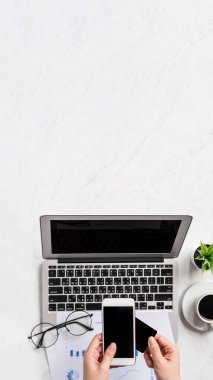 Bir kadın çevrimiçi ödeme ya da alışveriş yapıyor, ofis masasında kredi kartı ve cep telefonu taklidi yapıyor güzel moda mermer arka plan, üst görünüm, düz alan, telif alanı.