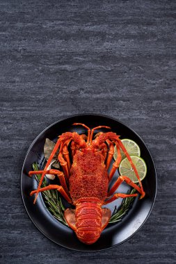 Top view of cooked boiled lobster, delicious dinner seafood meal set with knife and fork on black stone slate background for Valentine's day concept.