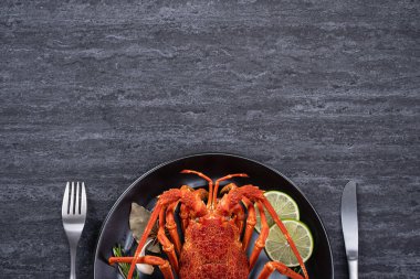 Top view of cooked boiled lobster, delicious dinner seafood meal set with knife and fork on black stone slate background for Valentine's day concept.
