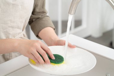 Close up of woman housekeeper is doing the dishes at home kitchen by using wash sponge and dishwashing.