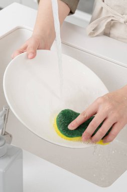 Close up of woman housekeeper is doing the dishes at home kitchen by using wash sponge and dishwashing.