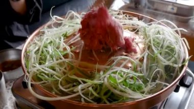 Seul 'deki Kore restoranında et ızgara bulgogi pişiriyorum. Bakır tavada taze Kore mutfağı ve dilimlenmiş yeşil soğan.