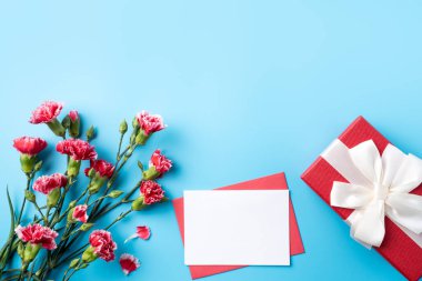 Anneler günü hediyesi. Üst görünüm tasarım tebrik kartı kavramı üzerinde kırmızı karanfil buketi olan parlak mavi masa arkaplanı