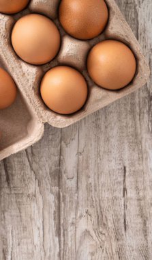 Tahta masa arkasındaki yumurta kutusundaki taze kahverengi tavuk yumurtalarının üst görüntüsü..