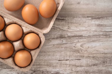 Tahta masa arkasındaki yumurta kutusundaki taze kahverengi tavuk yumurtalarının üst görüntüsü..