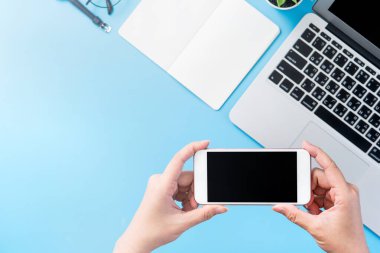 Bir kadın minimal mavi masa ile izole bir akıllı telefon tutuyor, online alışveriş ödeme kavramı, evde internet çalışması, e-ticaret, kopya alanı, düz yatıyordu, üst görünüm, alay