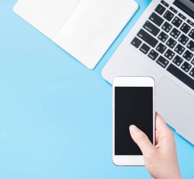 Bir kadın minimal mavi masa ile izole bir akıllı telefon tutuyor, online alışveriş ödeme kavramı, evde internet çalışması, e-ticaret, kopya alanı, düz yatıyordu, üst görünüm, alay