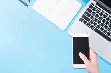 Bir kadın minimal mavi masa ile izole bir akıllı telefon tutuyor, online alışveriş ödeme kavramı, evde internet çalışması, e-ticaret, kopya alanı, düz yatıyordu, üst görünüm, alay