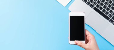 Bir kadın minimal mavi masa ile izole bir akıllı telefon tutuyor, online alışveriş ödeme kavramı, evde internet çalışması, e-ticaret, kopya alanı, düz yatıyordu, üst görünüm, alay