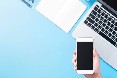 Bir kadın minimal mavi masa ile izole bir akıllı telefon tutuyor, online alışveriş ödeme kavramı, evde internet çalışması, e-ticaret, kopya alanı, düz yatıyordu, üst görünüm, alay