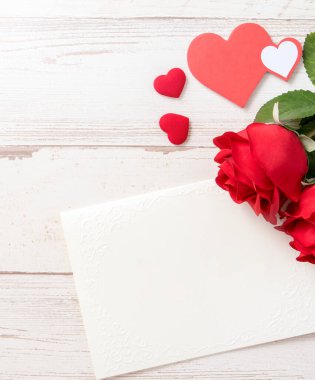 Selamlama konsepti - Parlak ahşap bir masaya izole edilmiş beyaz kart ile güzel güller ve kalpler, kopyalama alanı, düz yatış, üst manzara, taklit