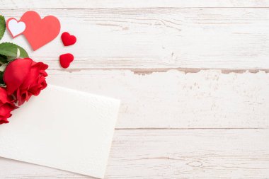 Selamlama konsepti - Parlak ahşap bir masaya izole edilmiş beyaz kart ile güzel güller ve kalpler, kopyalama alanı, düz yatış, üst manzara, taklit