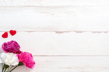 Anneler günü konsept fotoğrafçılığı - güzel karanfiller ve kalpler parlak ahşap bir masaya izole edilmiş beyaz bir kart, kopyalama alanı, düzlük, üst manzara, taklit