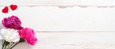 Anneler günü konsept fotoğrafçılığı - güzel karanfiller ve kalpler parlak ahşap bir masaya izole edilmiş beyaz bir kart, kopyalama alanı, düzlük, üst manzara, taklit