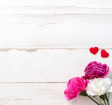 Anneler günü konsept fotoğrafçılığı - güzel karanfiller ve kalpler parlak ahşap bir masaya izole edilmiş beyaz bir kart, kopyalama alanı, düzlük, üst manzara, taklit