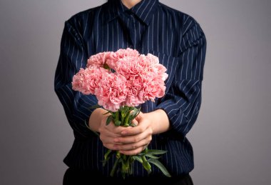 Koyu mavi çizgili gömlekli genç kız anneler günü konseptine hediye olarak bir demet güzel çiçek açan pembe karanfiller veriyor. Kapatın, kopyalayın, kırpın.