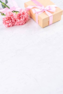 Anneler günü el yapımı hediye kutusu fikri, bebek pembe kurdeleli güzel karanfiller modern mermer masaya izole edilmiş, kapatın, kopyalayın, taklit edin