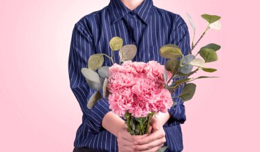 Koyu mavi çizgili gömlekli genç kız anneler günü konseptine hediye olarak bir demet güzel çiçek açan pembe karanfiller veriyor. Kapatın, kopyalayın, kırpın.