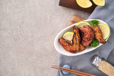 Kızarmış tatlı soslu teriyaki tavuk kanatlarının üst görüntüsü gri masa arkasında beyaz bir tabakta..