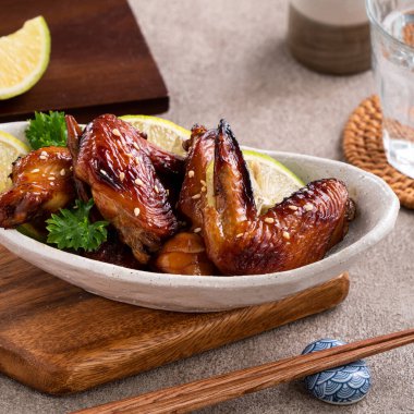 Kızarmış tatlı soslu teriyaki tavuk kanatlarını gri masa arkasında beyaz bir tabakta kapat..