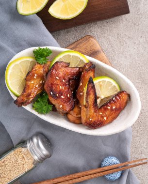 Kızarmış tatlı soslu teriyaki tavuk kanatlarının üst görüntüsü gri masa arkasında beyaz bir tabakta..