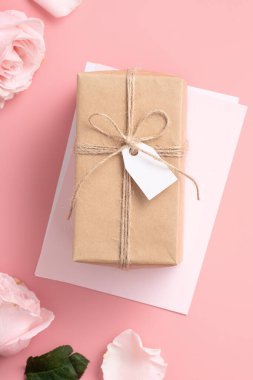 Pembe gül çiçekli Anneler Günü tasarım konsepti ve pembe masa arkasında paketlenmiş Kraft hediye kutusu..