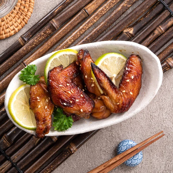 Kızarmış tatlı soslu teriyaki tavuk kanatlarının üst görüntüsü gri masa arkasında beyaz bir tabakta..