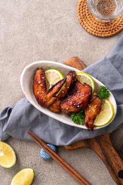 Kızarmış tatlı soslu teriyaki tavuk kanatlarının üst görüntüsü gri masa arkasında beyaz bir tabakta..