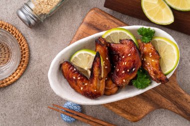 Kızarmış tatlı soslu teriyaki tavuk kanatlarının üst görüntüsü gri masa arkasında beyaz bir tabakta..