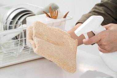 Kadın ev hanımı, tezgahın yüzeyini silmek için bez parçası ve şişe temizleyicisiyle bahar temizliği yapıyor..